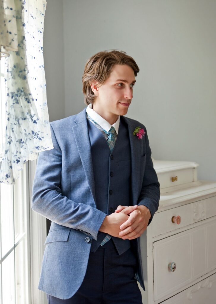groom leaning on bookcase waiting for wedding to start